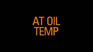 Icône orange de témoin d’alerte de la température de l’huile de transmission sur boîte automatique avec texte « AT OIL TEMP » sur fond noir.