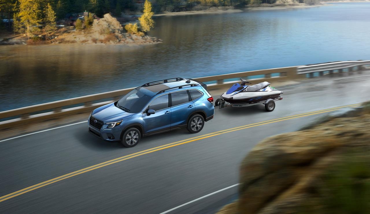 vue latérale avant d'une Subaru Forester 2024 remorquant un bateau sur une route de campagne longeant un lac