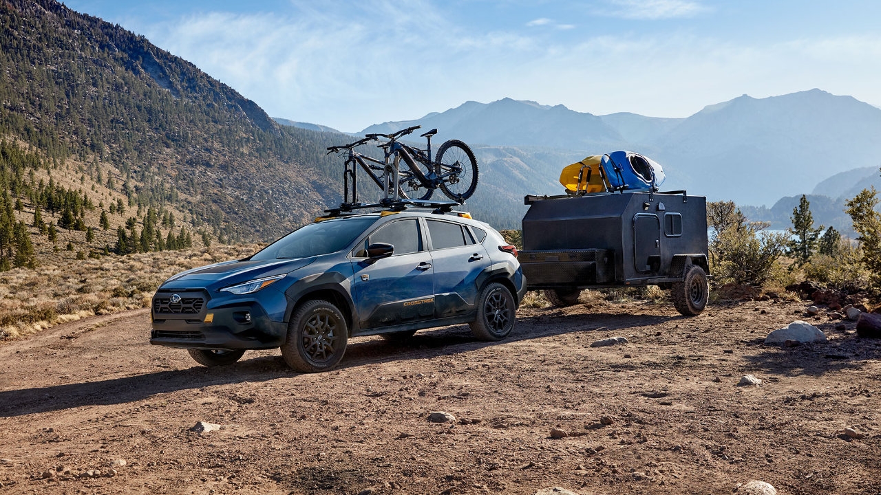 vue latérale avant d'un Subaru Crosstrek Wilderness 2025 remorquant une petite remorque sur une route de montagne