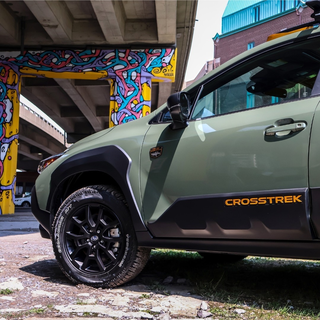 Subaru Crosstrek Wilderness 2025 vert alpin garé sous un viaduc urbain coloré, vue latérale avant droite.